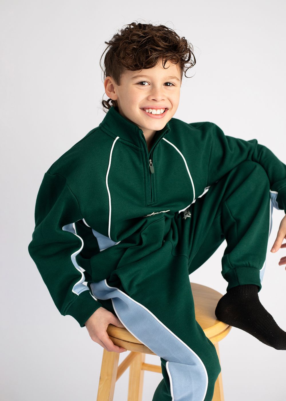 Child wearing a green quarter-zip sweatshirt poses playfully on a white background.