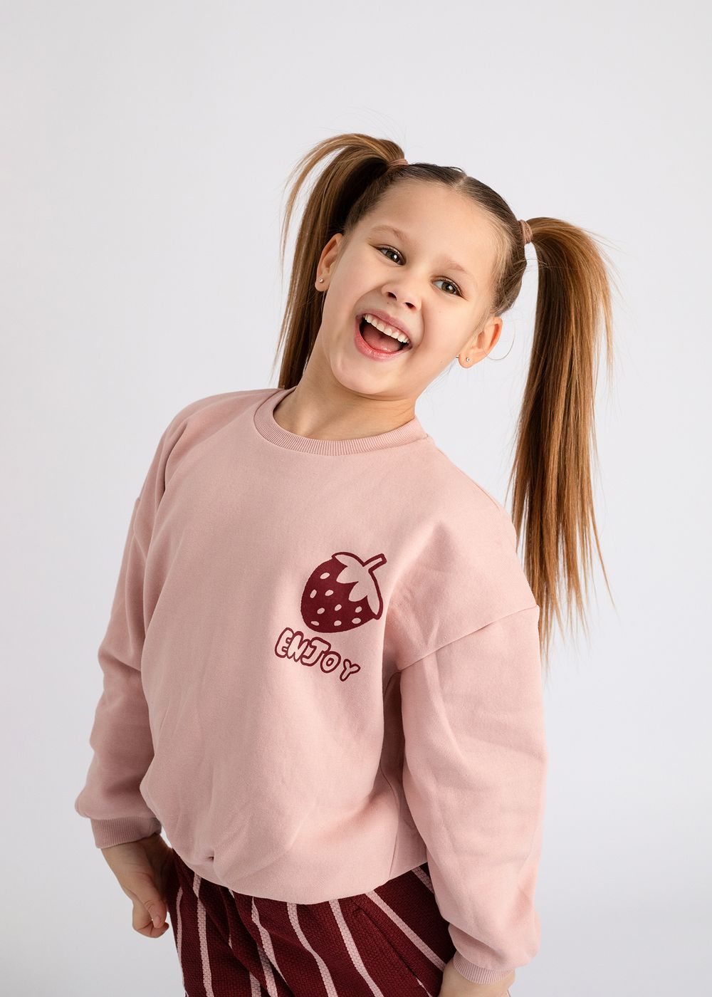 A child wearing a pink sweatshirt with a mushroom graphic design shows various playful poses against a white background.