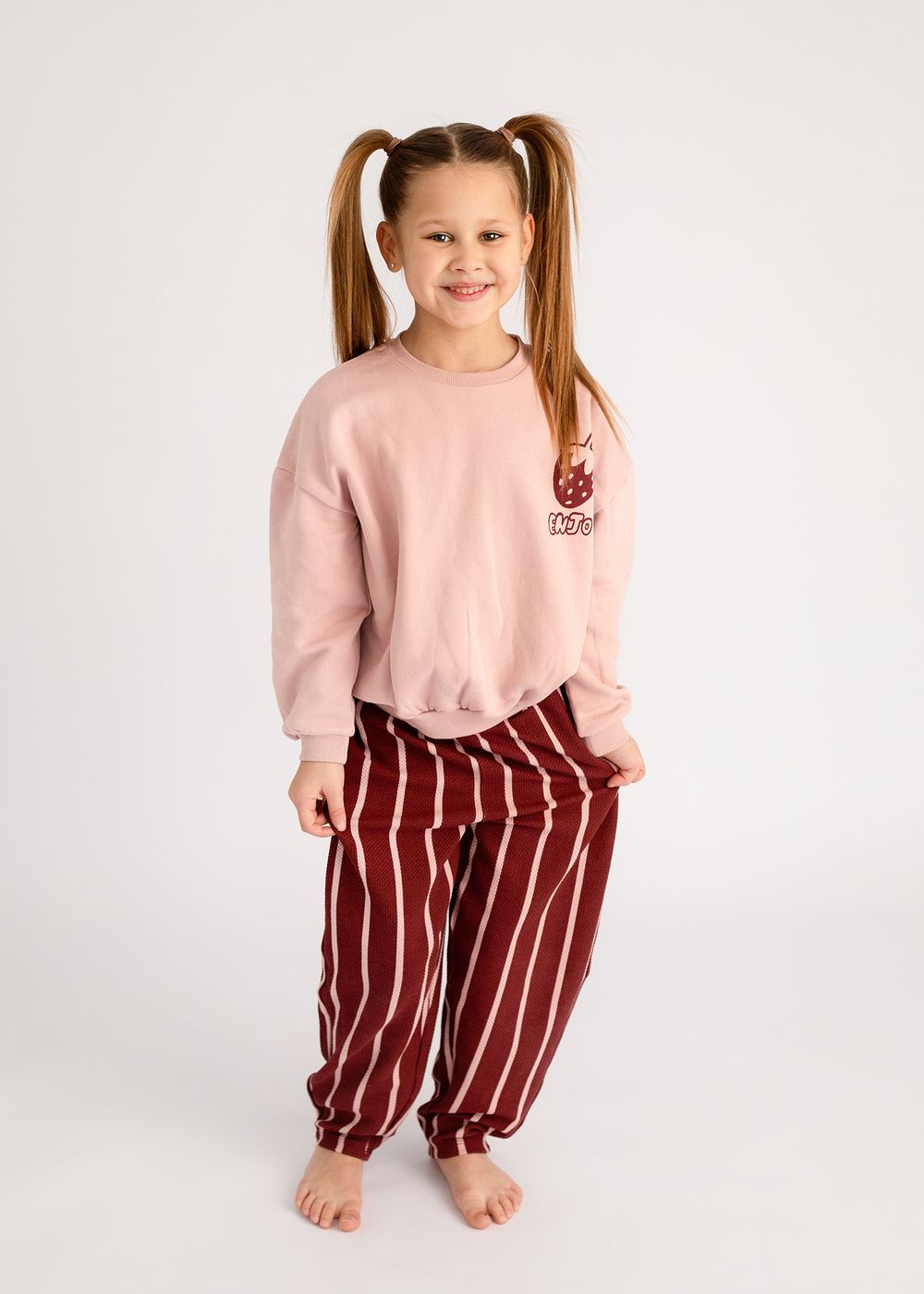 A child wearing a pink sweatshirt and burgundy striped pants poses in four different playful stances against a white backdrop.