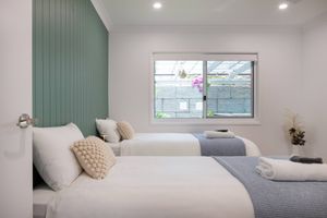 Modern bedroom with twin beds, mint green accent wall, and white linens featuring natural light from window.