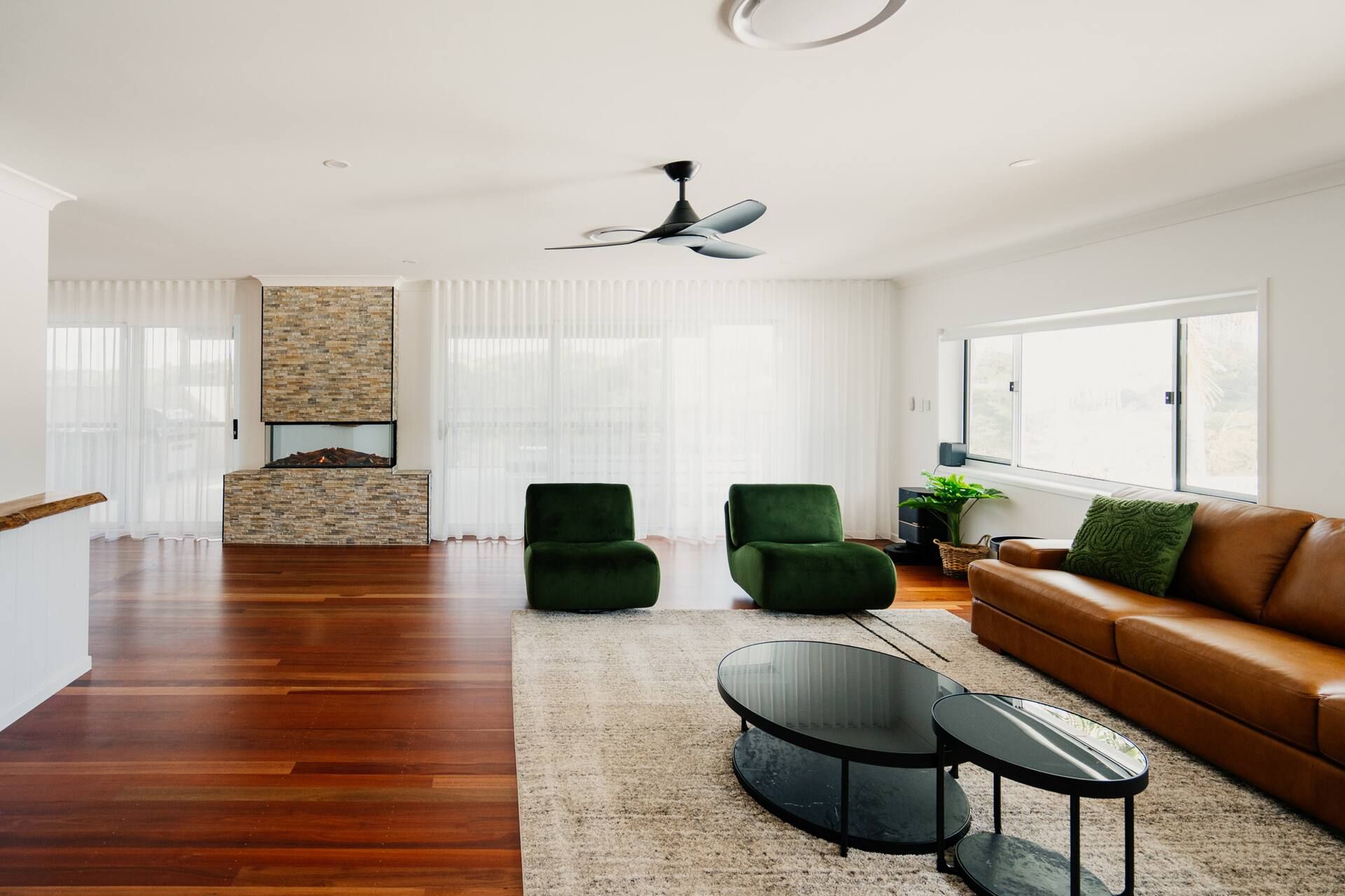 Spacious living room with stone fireplace, green velvet chairs, and brown leather sofa on polished wood floors.