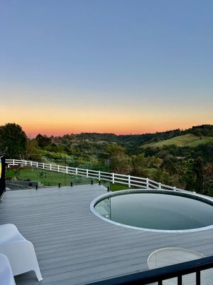 Luxurious deck with circular hot tub overlooking scenic hills and countryside at sunset with white fence and warm sky.