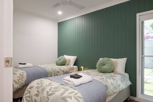 Modern bedroom with two single beds featuring green accent wall, floral bedding, and sage throw pillows.