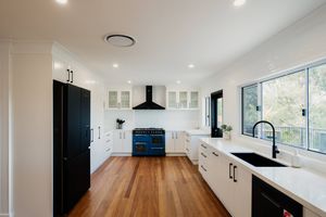 Contemporary white kitchen with blue range, hardwood floors and large windows offering natural light.