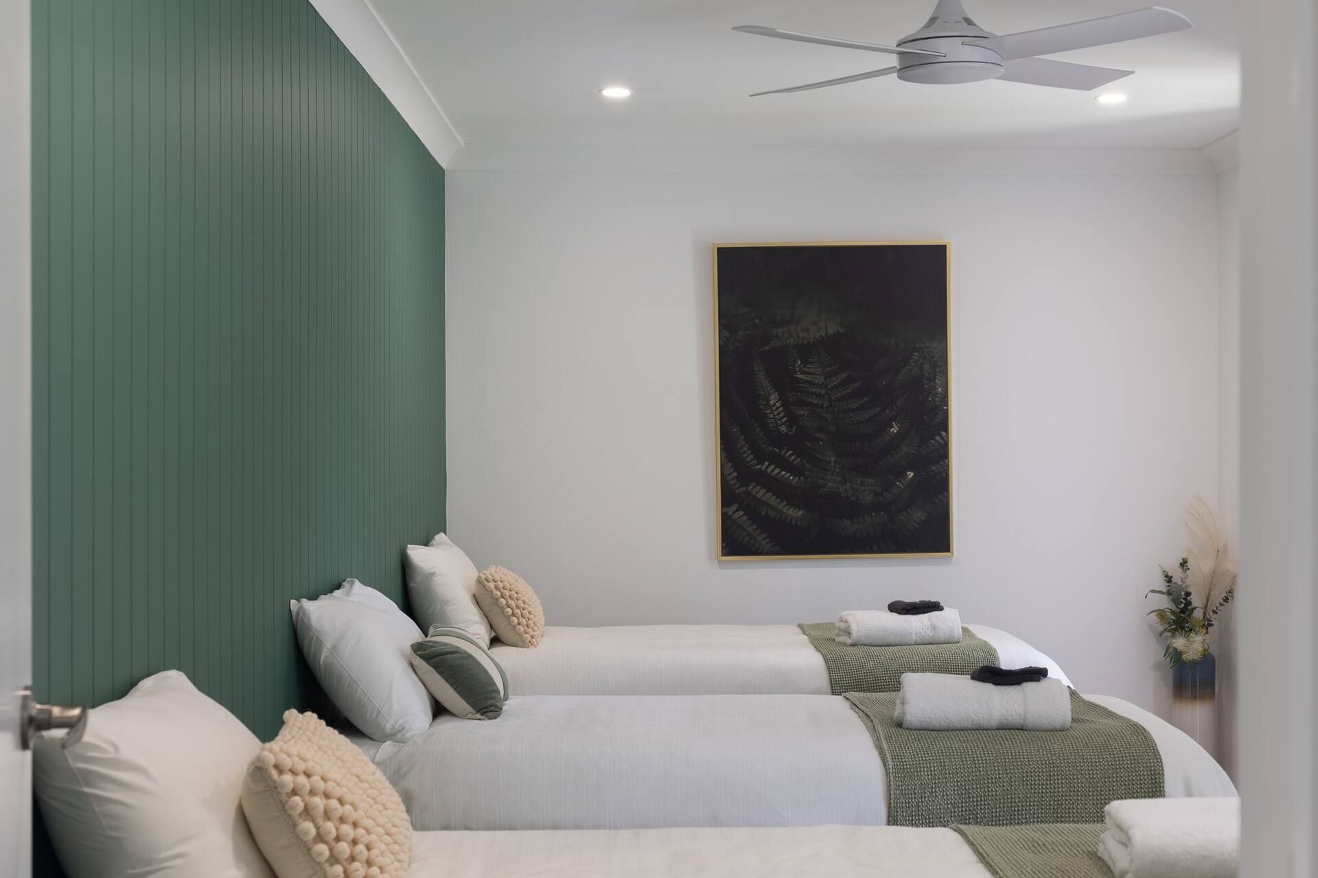 Modern bedroom with green accent wall, white bedding, and ceiling fan showcasing contemporary minimalist design.