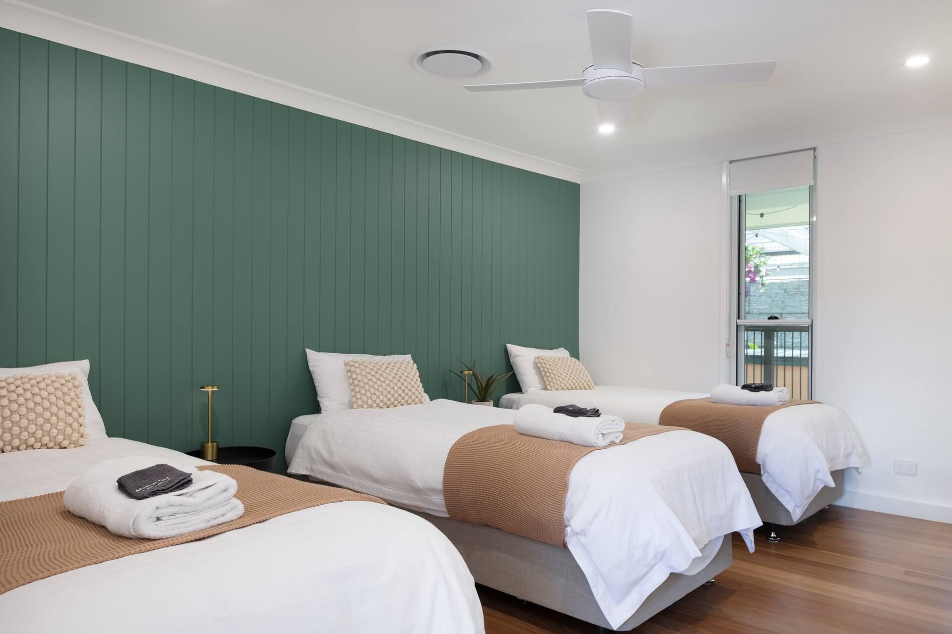 Modern bedroom interior with dark green accent wall, white bedding, and recessed lighting.