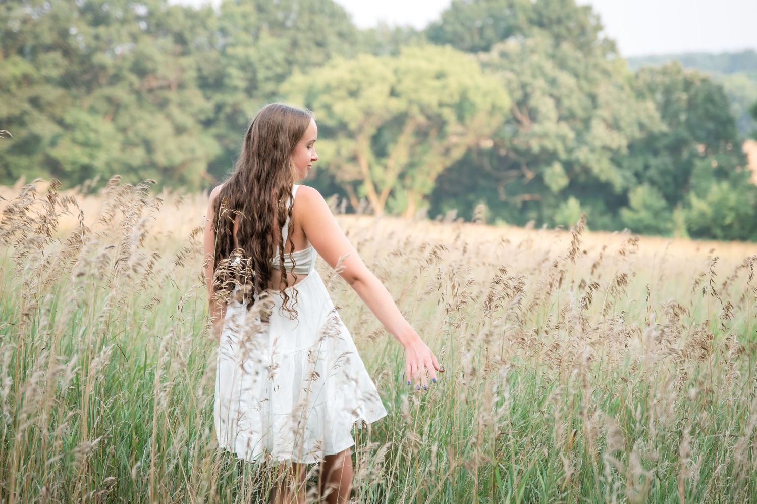 A white lace dress flows in the breeze as someone walks through a golden summer meadow of tall grass.