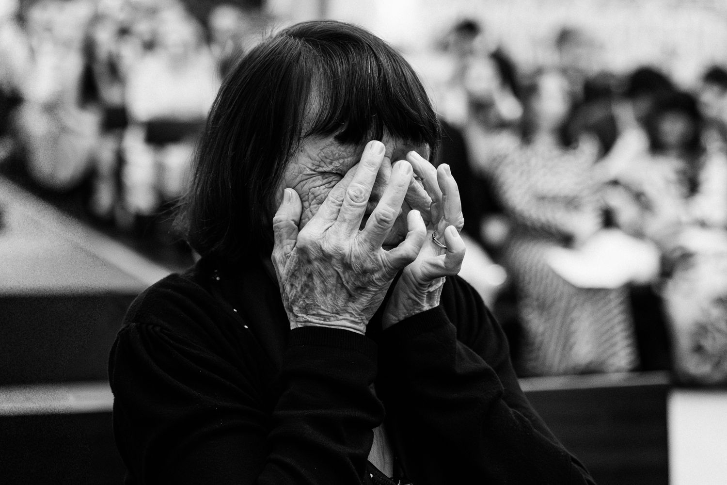 A black and white image shows a person with their hands covering their face, appearing distressed or emotional.
