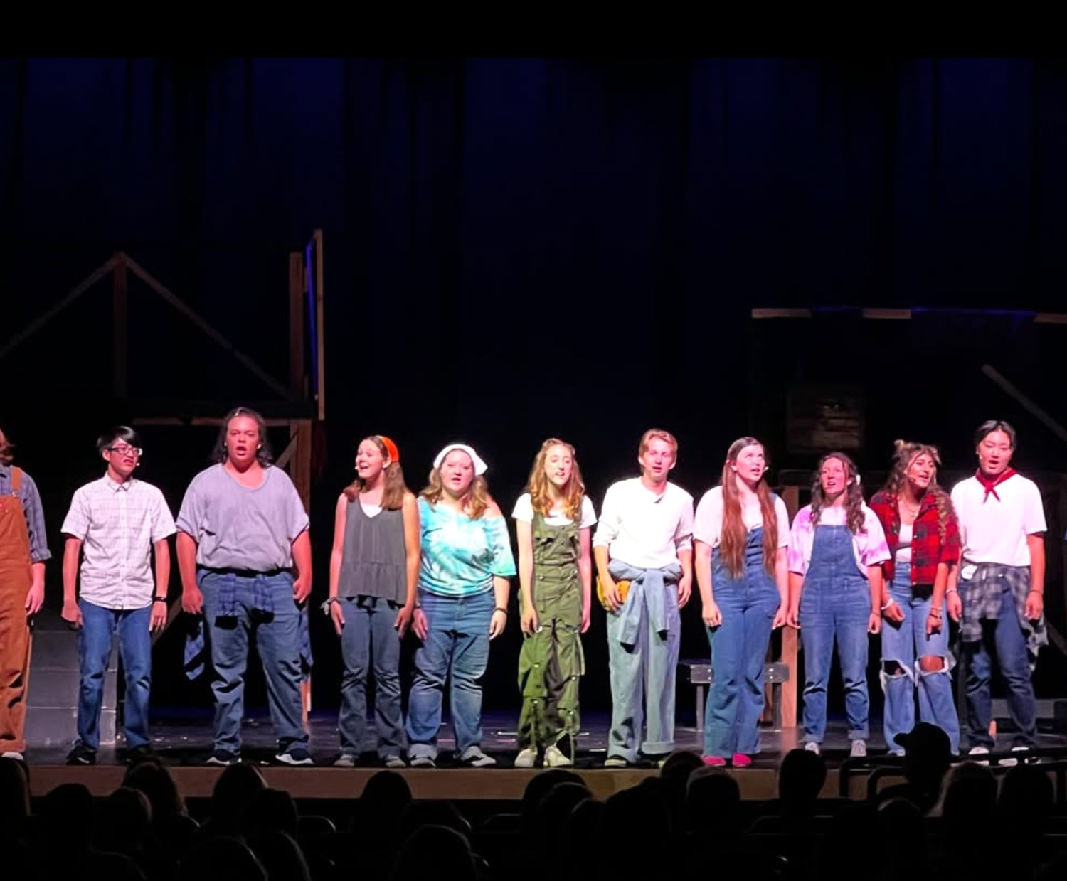 A cast of student performers takes a bow on stage in casual costumes during a school musical.
