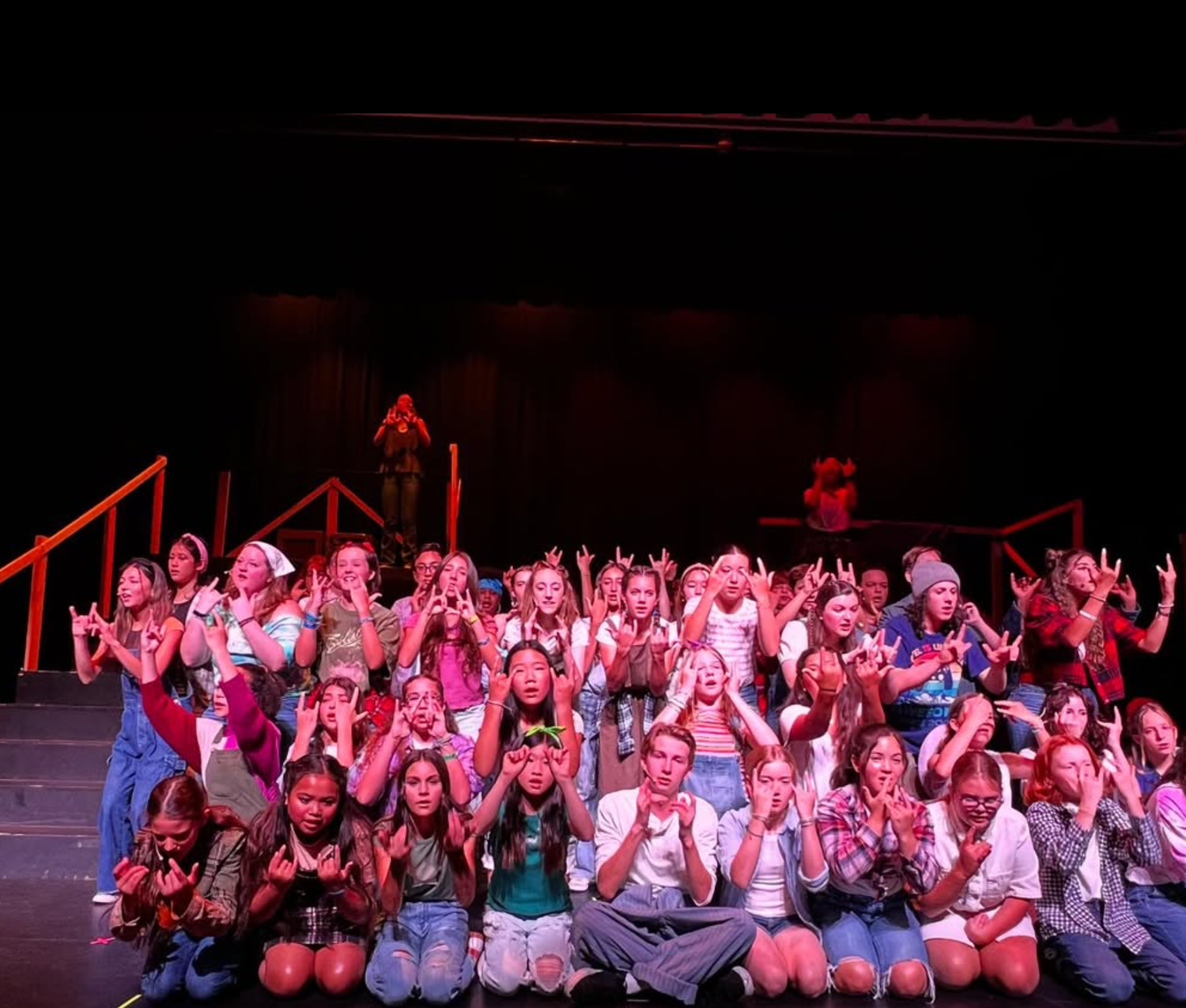 Large group of children posing on stage making rock gestures during a theatrical performance.