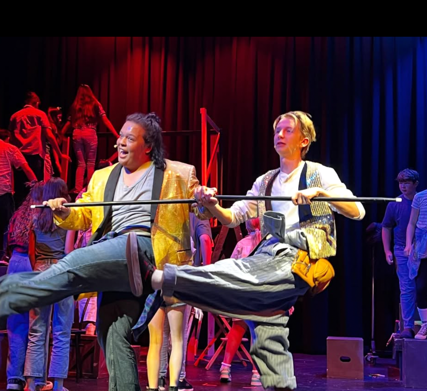 Two actors perform a comedic scene with a third actor on stage during a play.