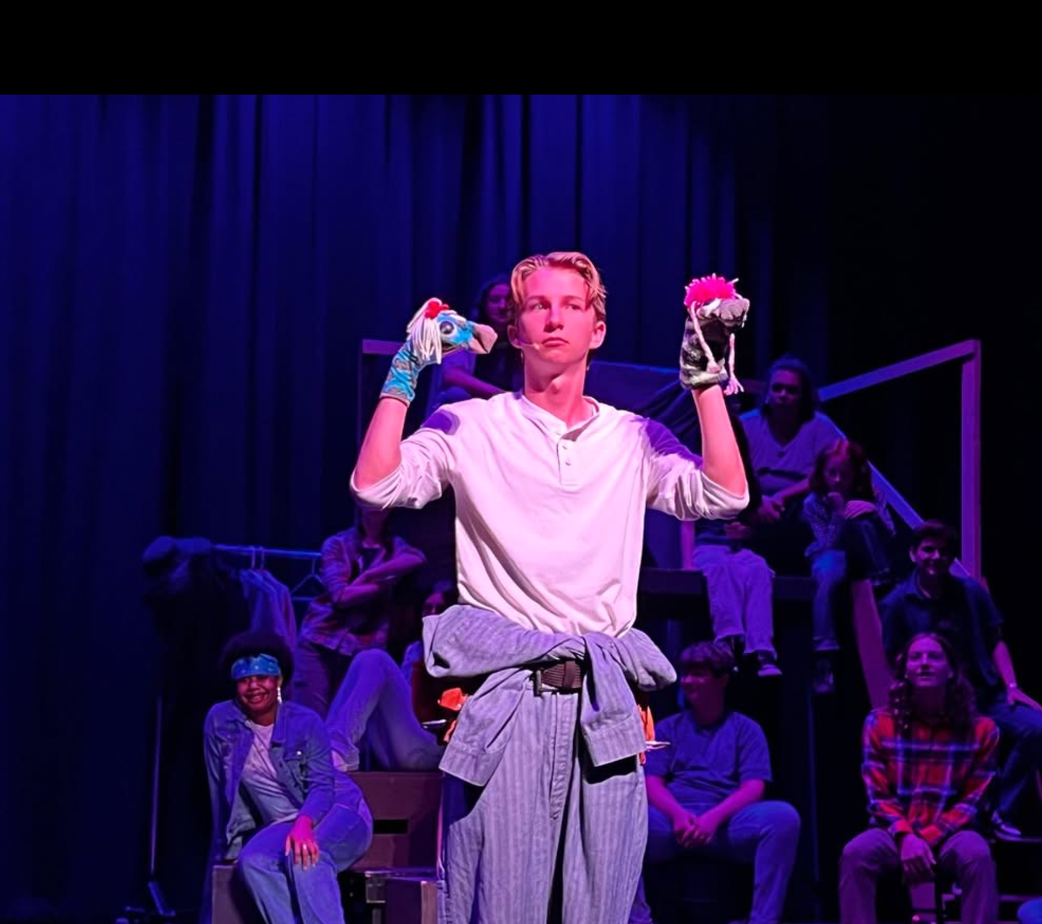 Young male actor holds colorful props on stage during a theatrical production.