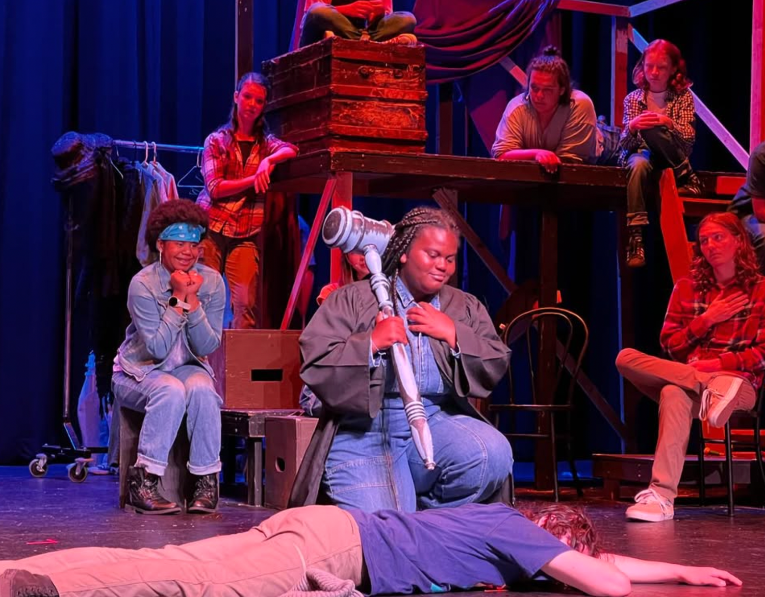 Student actress holds a hair dryer prop on stage during a dramatic theater performance.