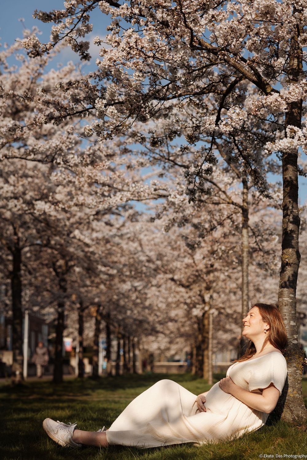 A dreamy spring scene with cherry blossoms blooming over a white dress against green grass.