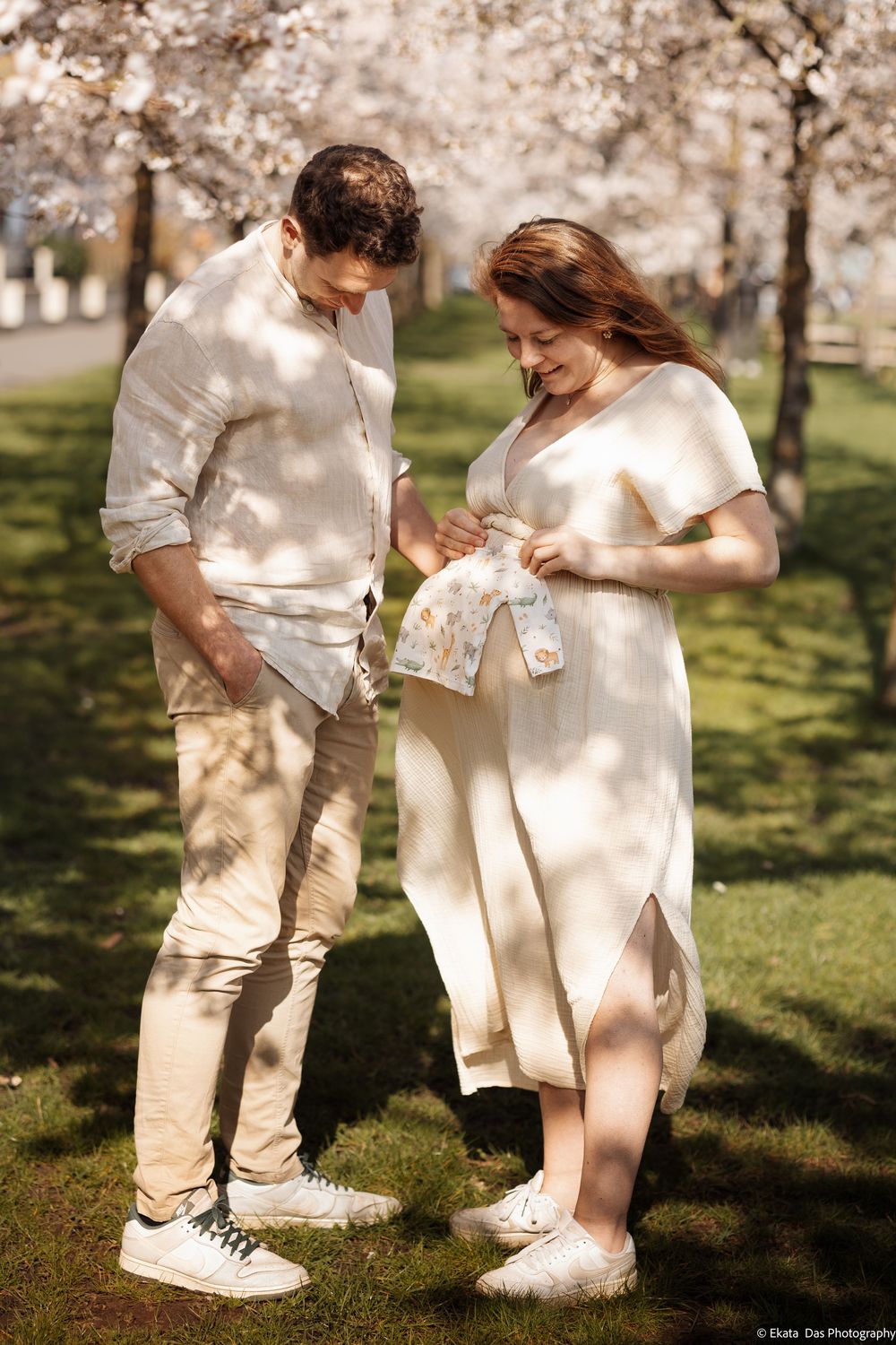 Couple in light colored outfits sharing tender moments under blooming cherry trees.