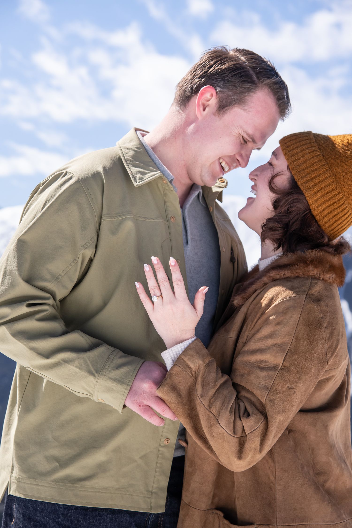 A couple in winter clothing share an intimate moment against a cloudy sky background for an Aspen Colorado engagement photo session.