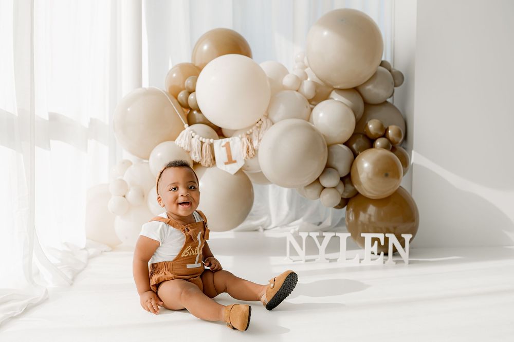 Neutral toned baby photography studio setup with beige balloons and soft white backdrop for milestone photos.