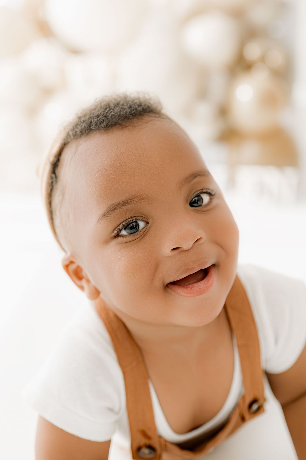 Close up portrait of a smiling baby with bright eyes against a light background.