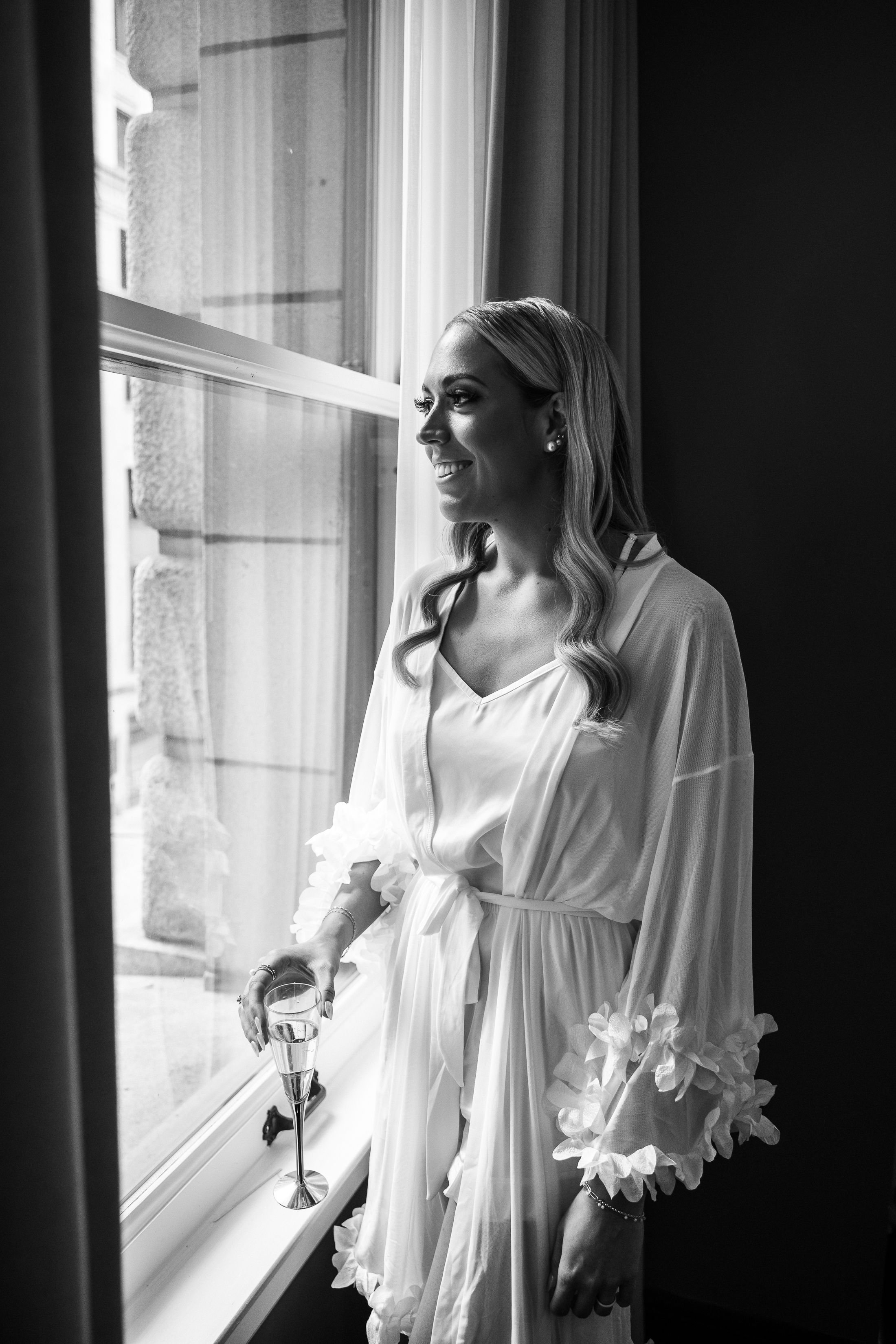 Black and white portrait of figure in white silk robe standing by window in natural light.