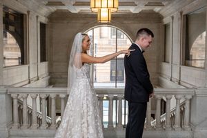 A wedding couple shares an intimate moment in an elegant marble hallway with ornate architectural details and warm lighting.