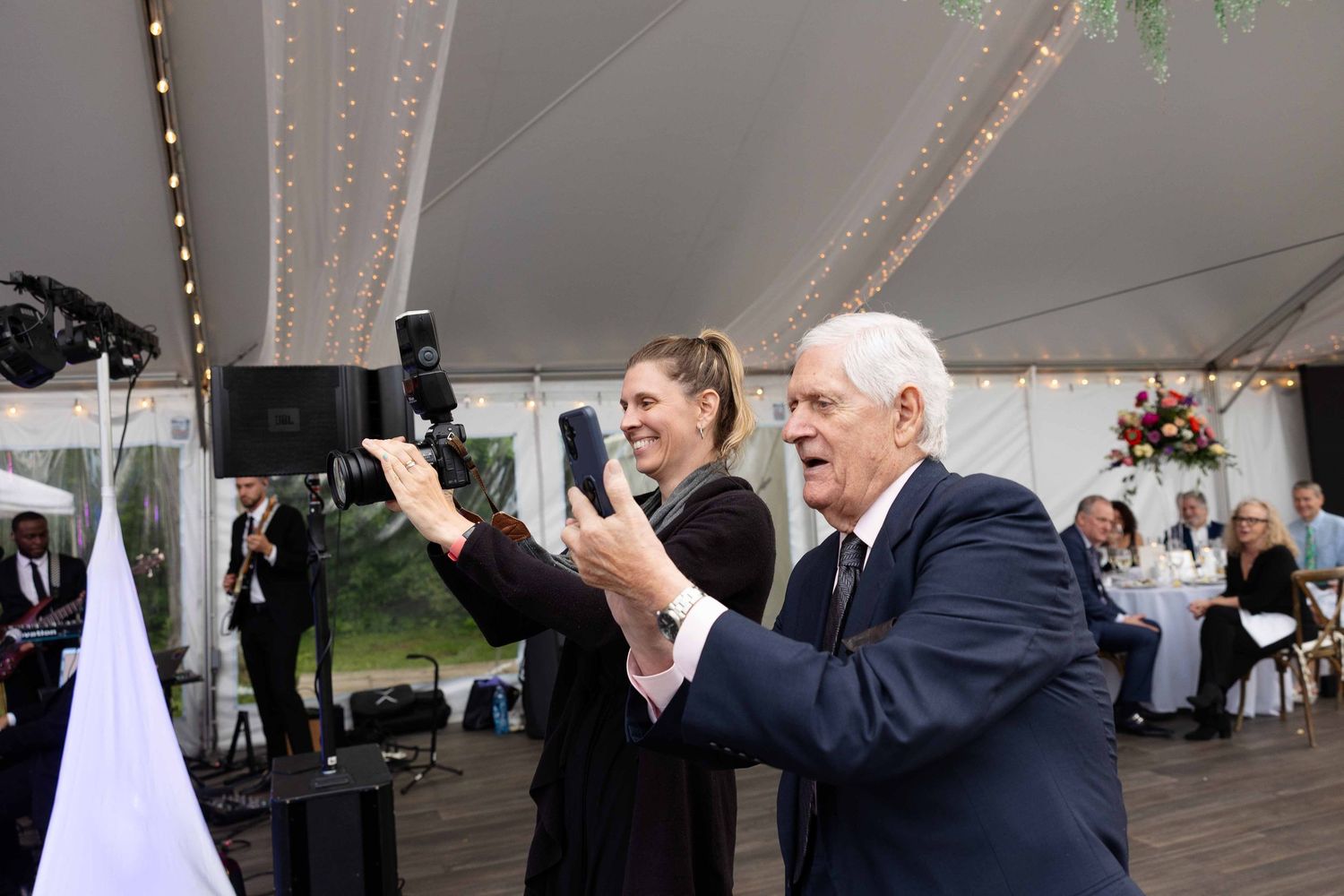 Wedding guests dance and celebrate under an elegant white tent with string lights at an outdoor reception.