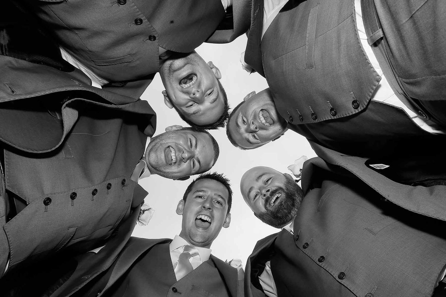 Black and white low angle view of a group huddled in a circle looking down at the camera, creating a playful composition.