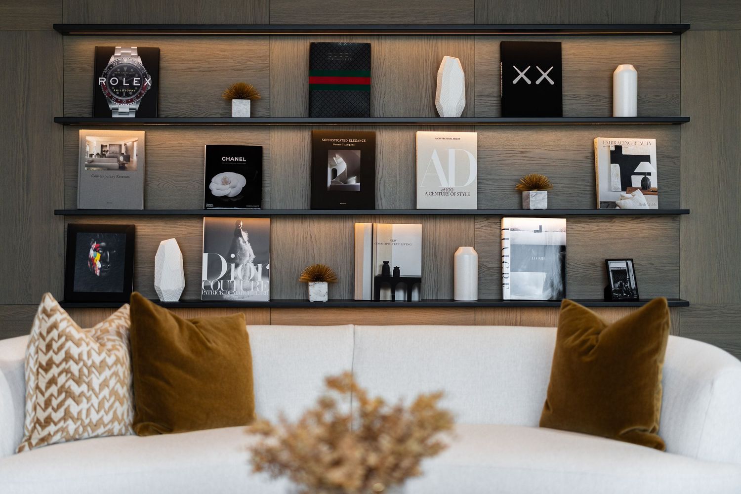 Modern living room features dark floating shelves decorated with books and decor against a gray wall.