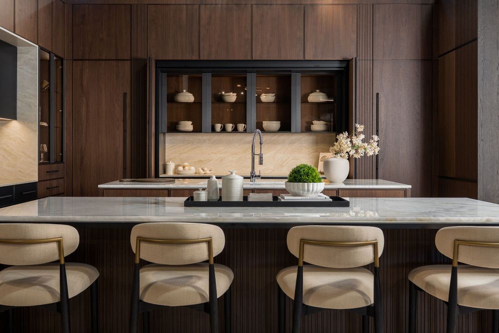 Modern luxury kitchen with dark wood cabinets, marble countertops, and cream-colored bar stools in a contemporary home.