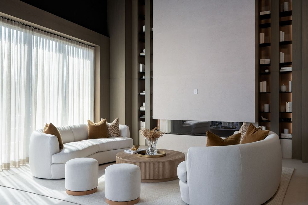 Contemporary open-plan lounge area featuring white curved furniture and floor-to-ceiling windows.