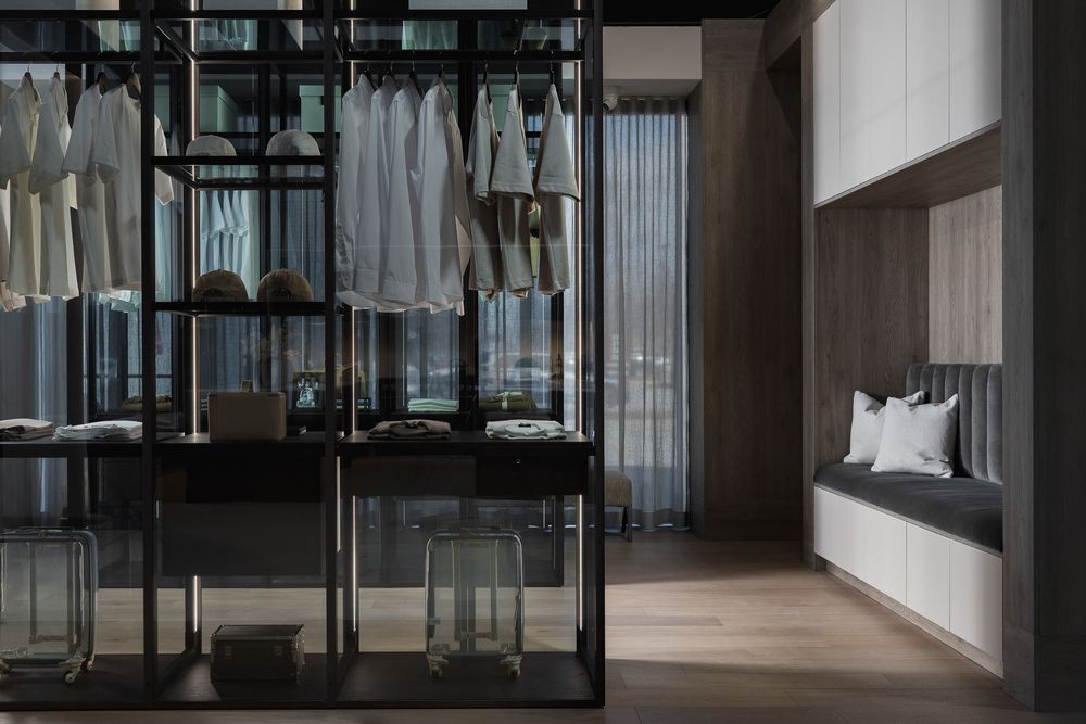 Modern walk-in closet with glass panels and hanging clothes in neutral tones.