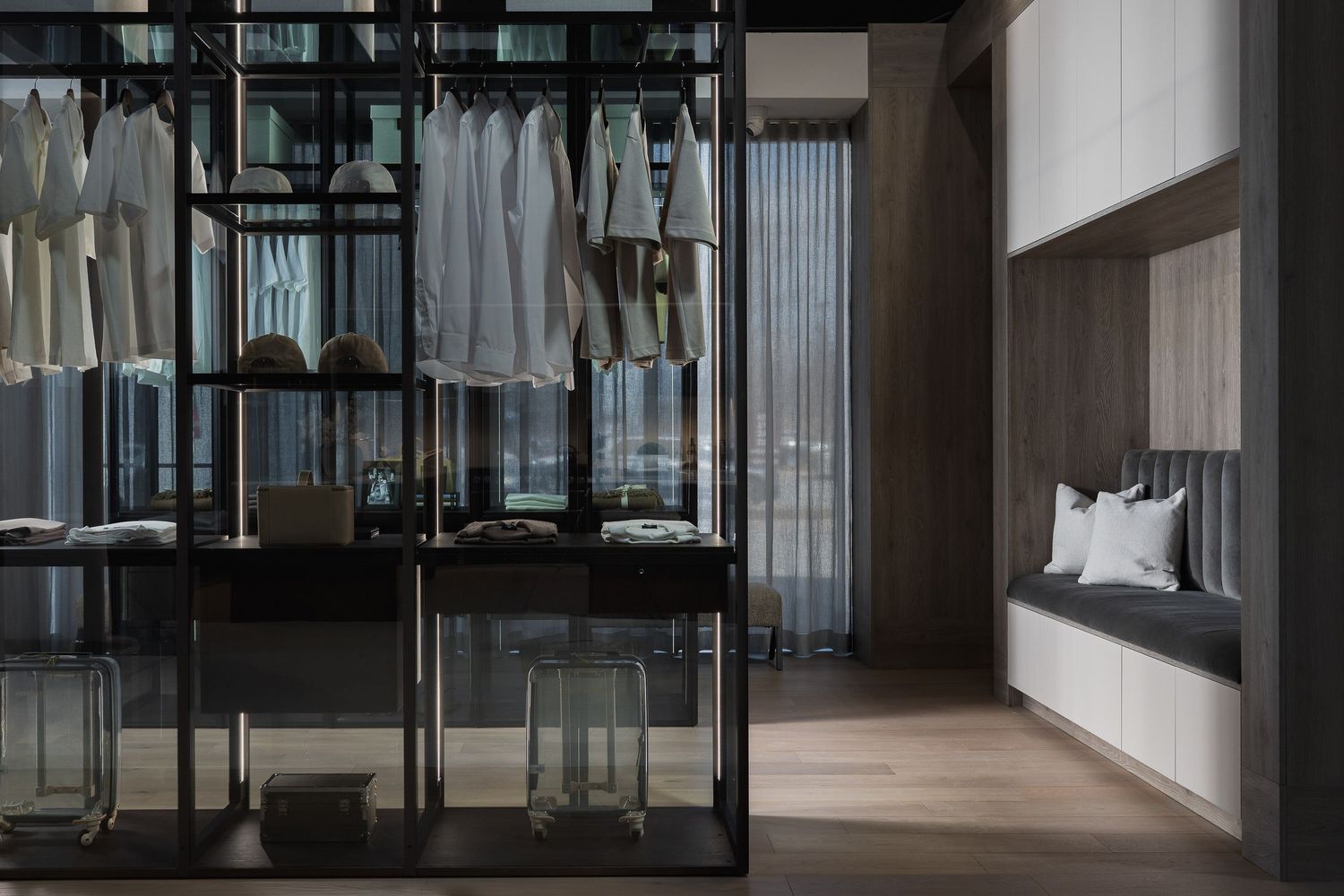 Modern walk-in closet with glass panels and hanging clothes in neutral tones.