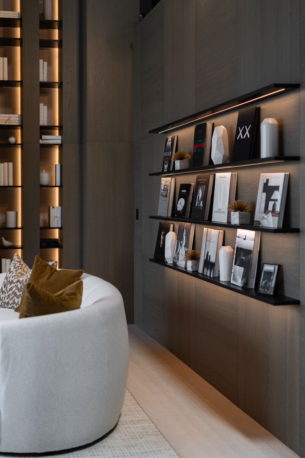 Modern living room interior with dark walls featuring illuminated shelving displaying framed photographs and decor items.