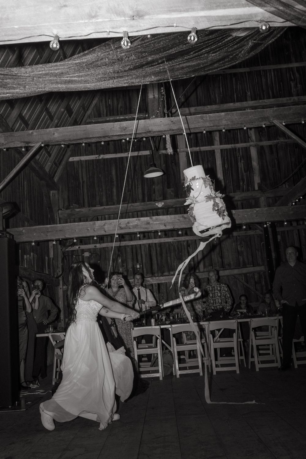 Black and white sequence shows a bride swinging on a rope swing in a rustic barn venue during a wedding reception.