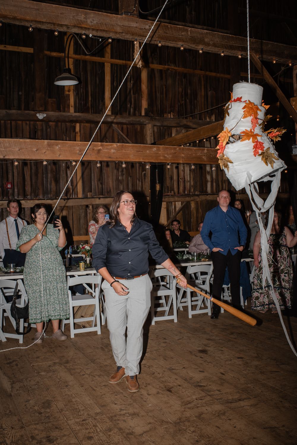 People enjoying a fun wedding reception game with suspended objects in a rustic barn setting.