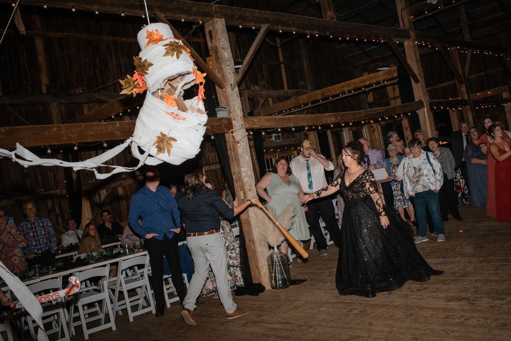 Guests gather around for entertainment at a barn wedding reception with string lights overhead.