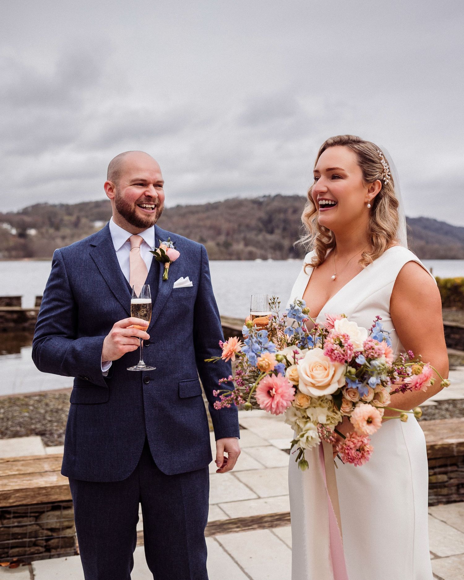 A couple shares a joyful moment on their wedding day at a scenic overlook with mountains and water in the background.