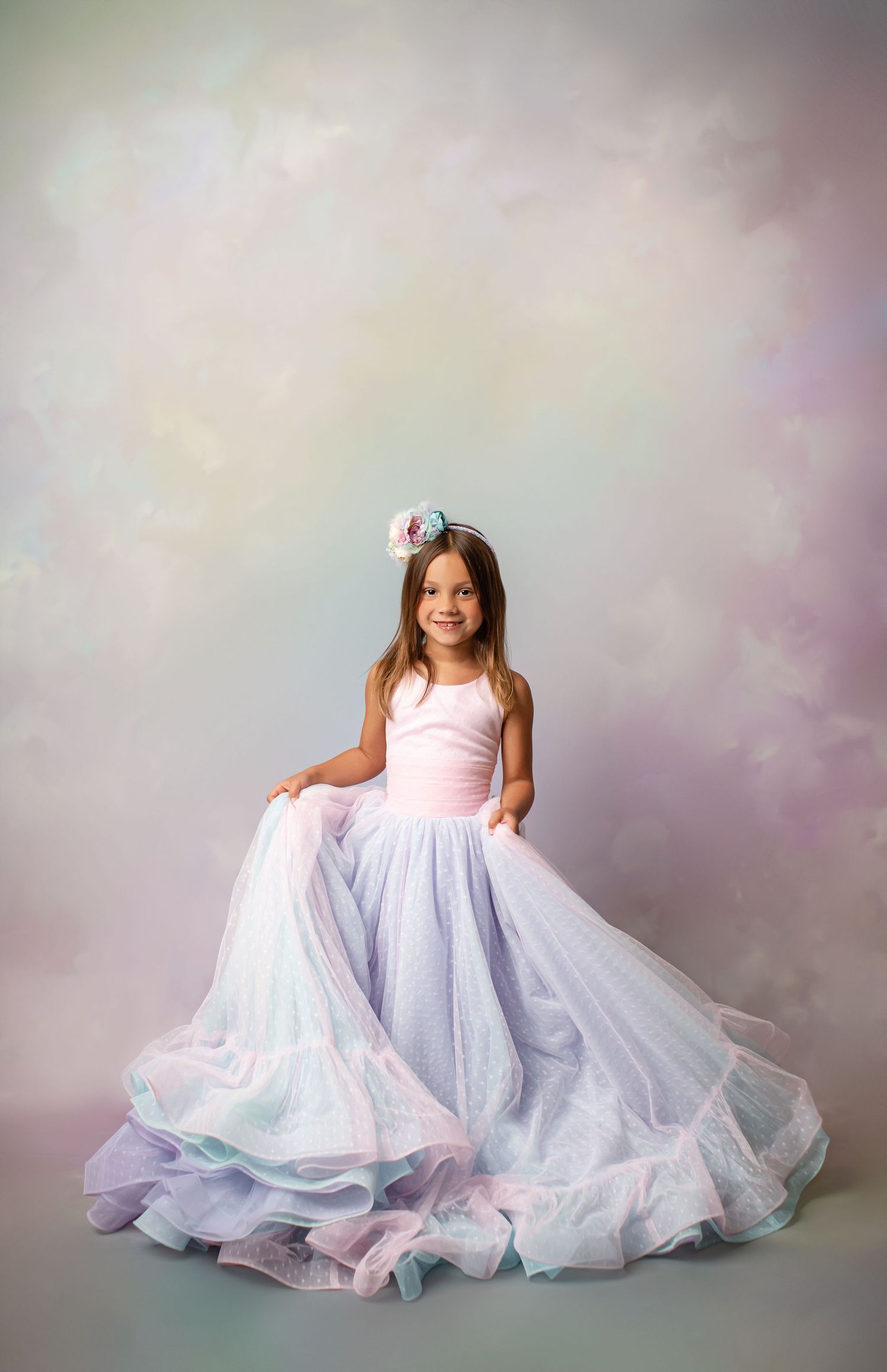 Young dancer in a white tulle dress and tiara poses gracefully barefoot against a bokeh backdrop.
