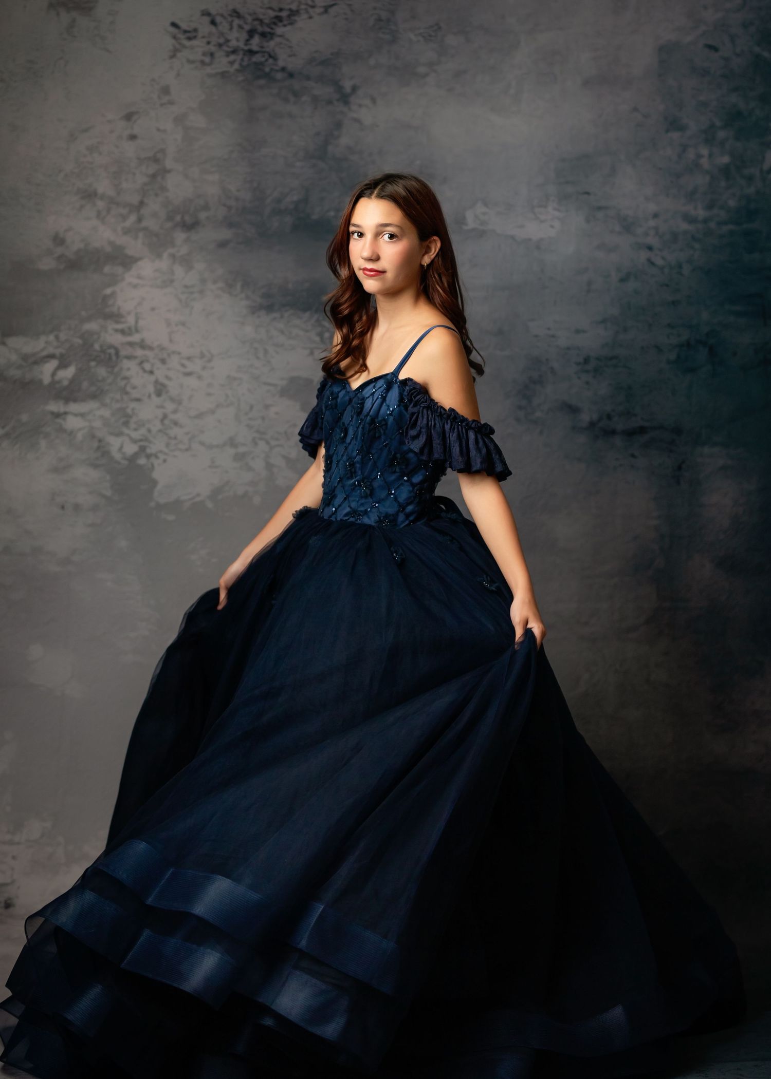 A flowing purple ball gown with layers of tulle and a velvet bodice glows beautifully against a soft purple backdrop.