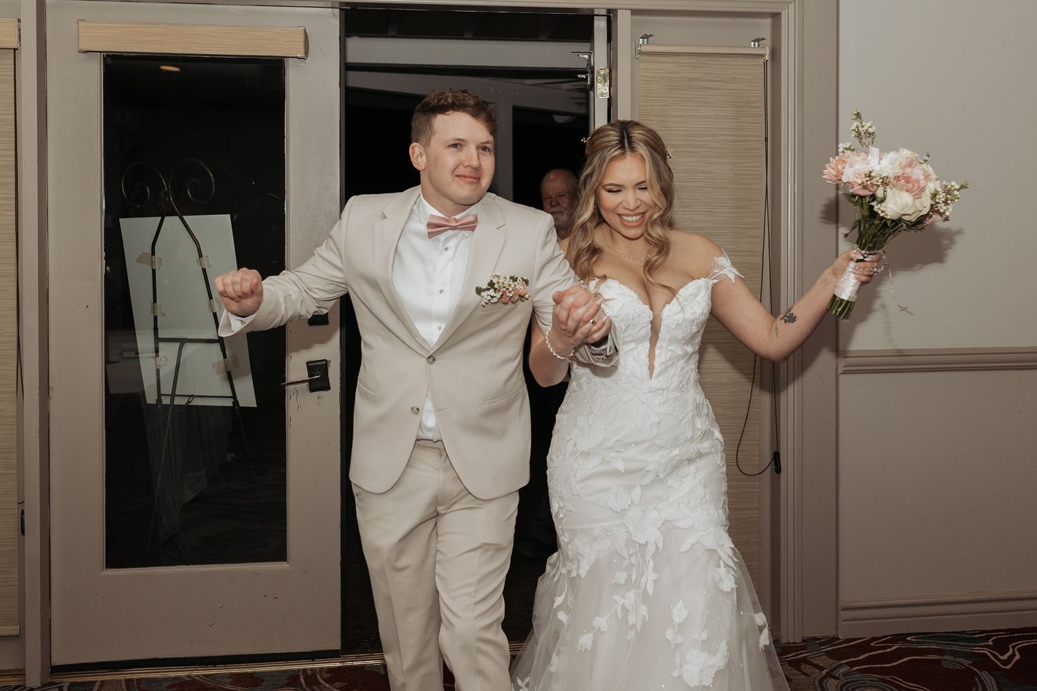 A couple in formal wedding attire shares a joyful moment while entering together at a reception at Singing Hills Golf Resort.