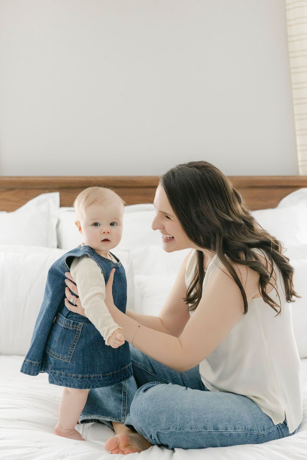 Parent and baby in matching denim share tender moments while relaxing on white bedding.