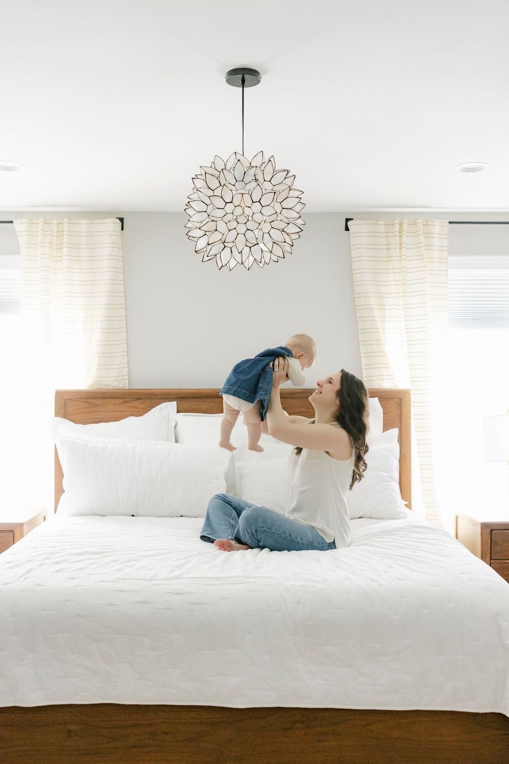 Modern white bedroom interior with stylish pendant light and people playing on a comfortable bed.