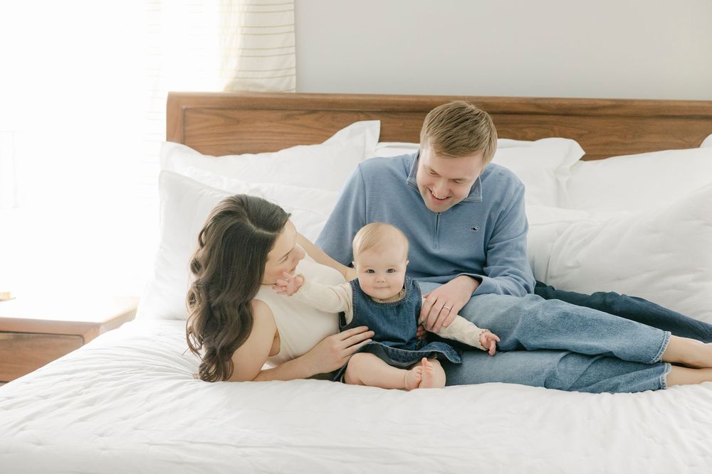 Family members laying together and relaxing on white bedding while sharing intimate moments at home.