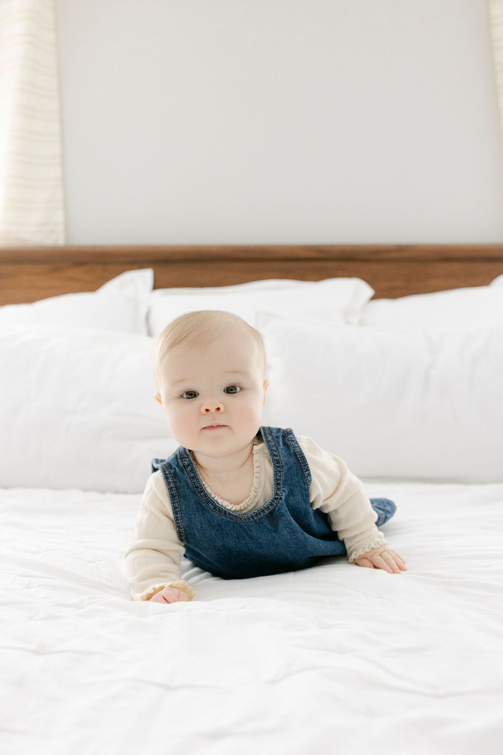 Baby wearing navy blue jumper lying on white bedding in bright natural light.