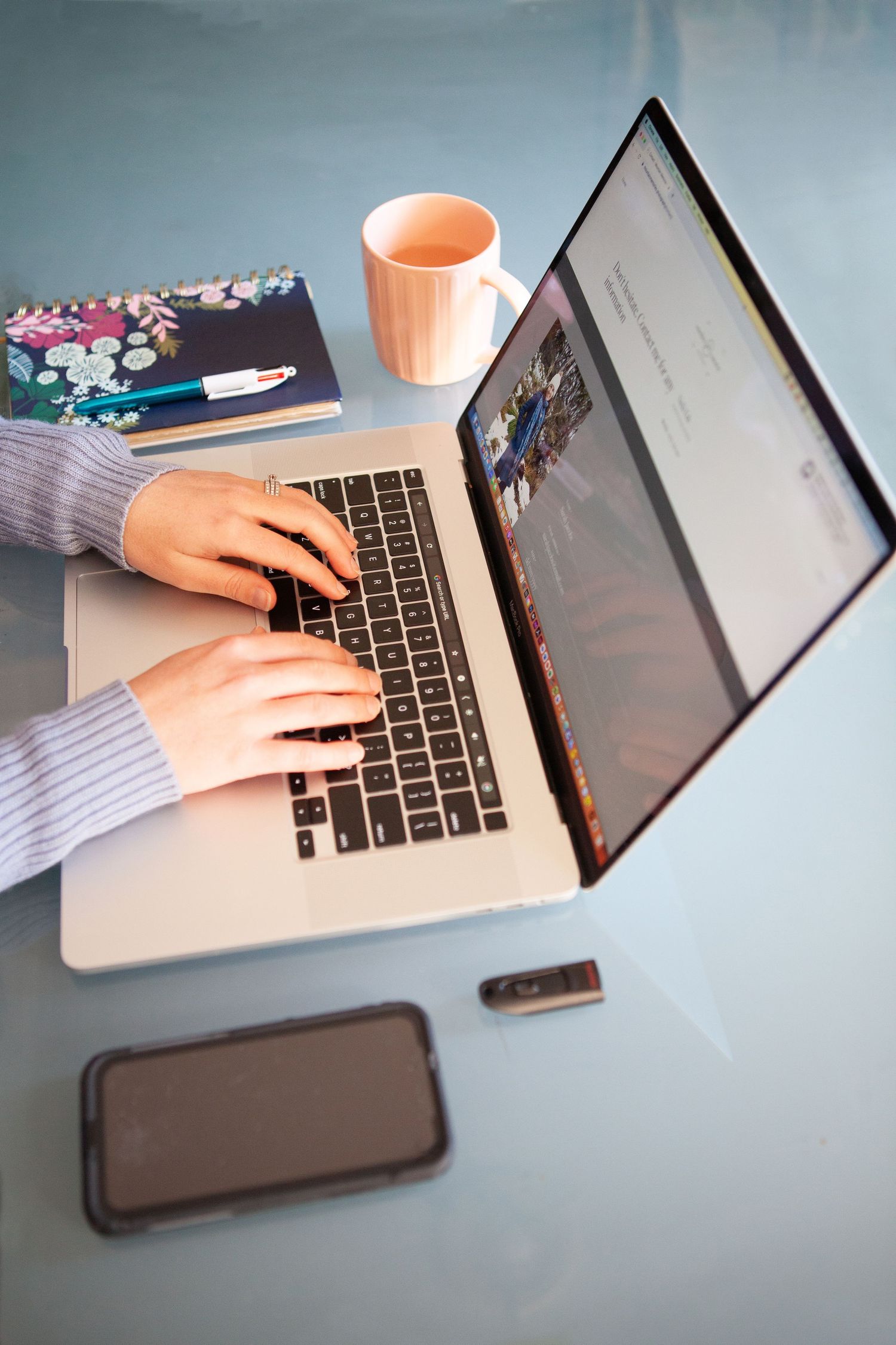Overhead view of hands typing on laptop with orange coffee cup nearby.