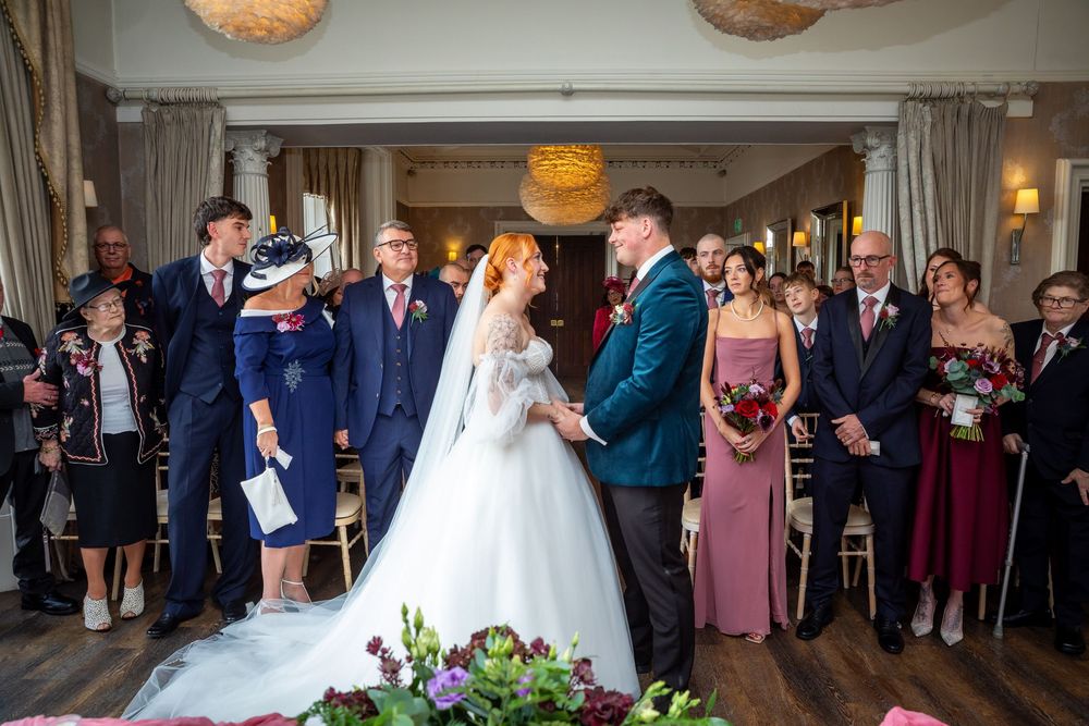 Bride and groom exchange vows surrounded by guests in a beautifully decorated wedding ceremony room.