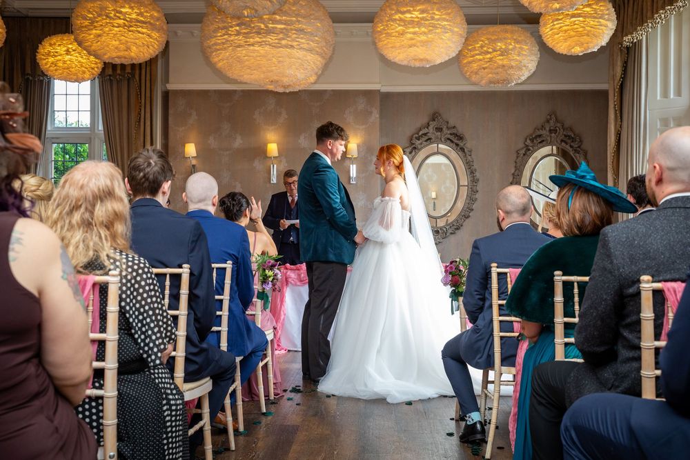 Bride and groom stand at altar before seated guests beneath warm globe pendant lights.