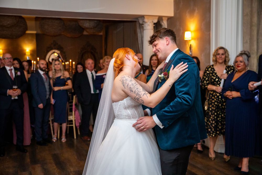 Bride and groom share first dance at elegant wedding reception while guests watch in background.