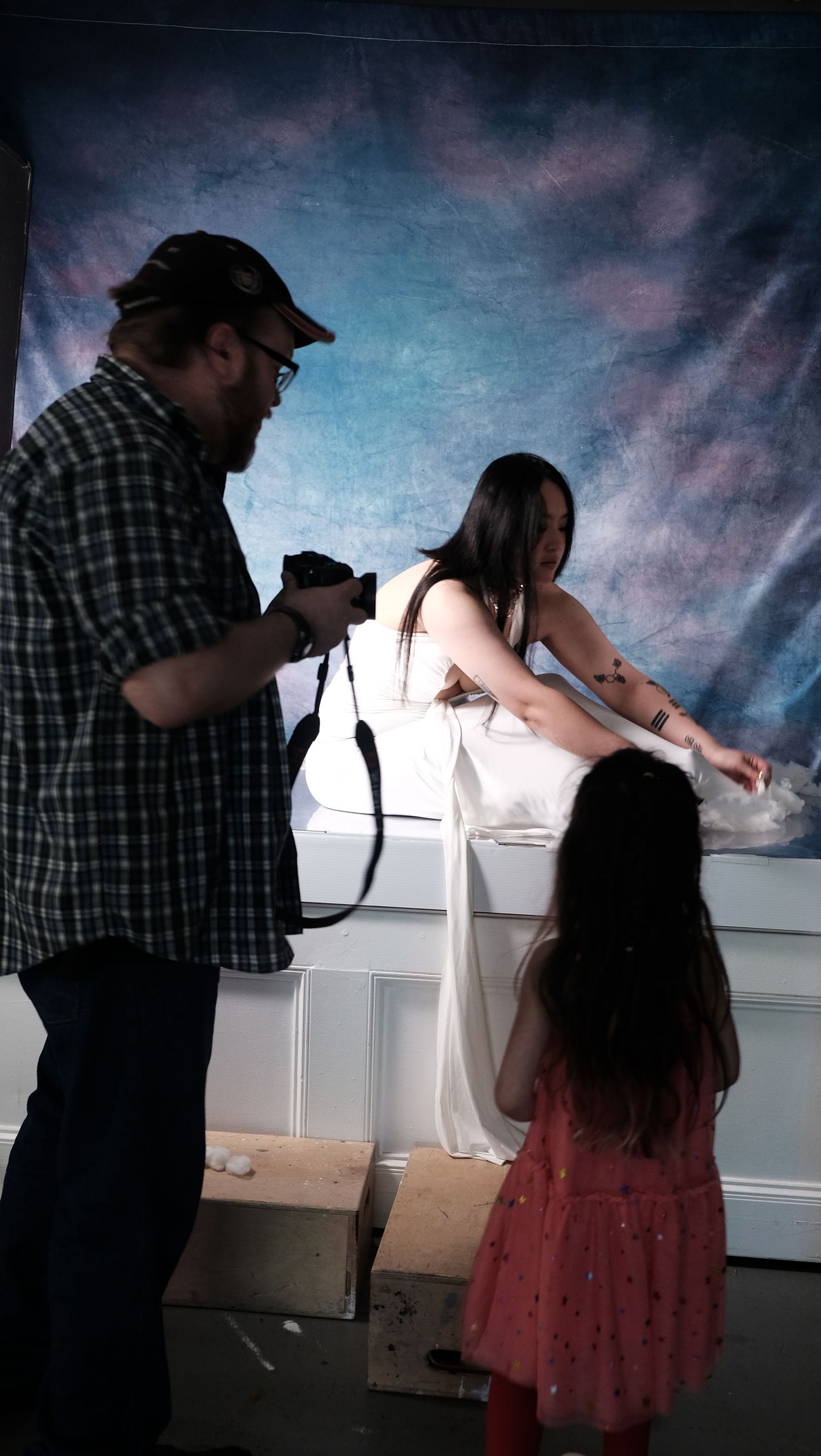 Behind the scenes photo of a photography session in a studio with a painted backdrop and white wainscoting.
