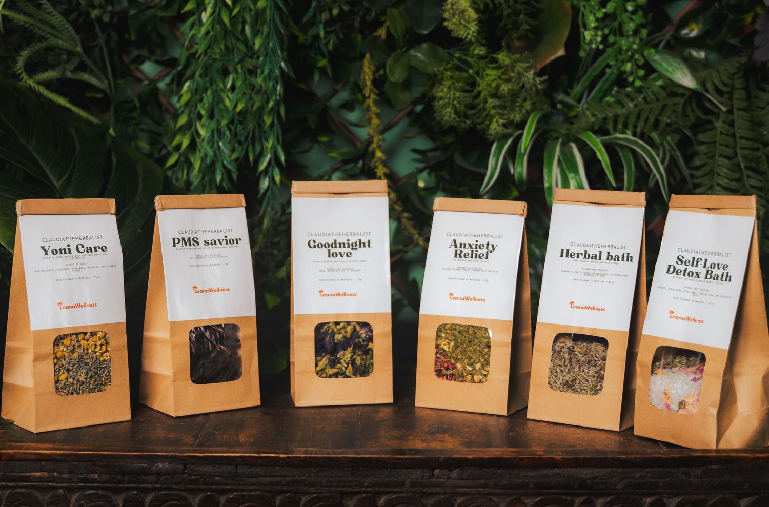 A row of kraft paper bags containing loose leaf teas displayed on a wooden surface with plants in background.