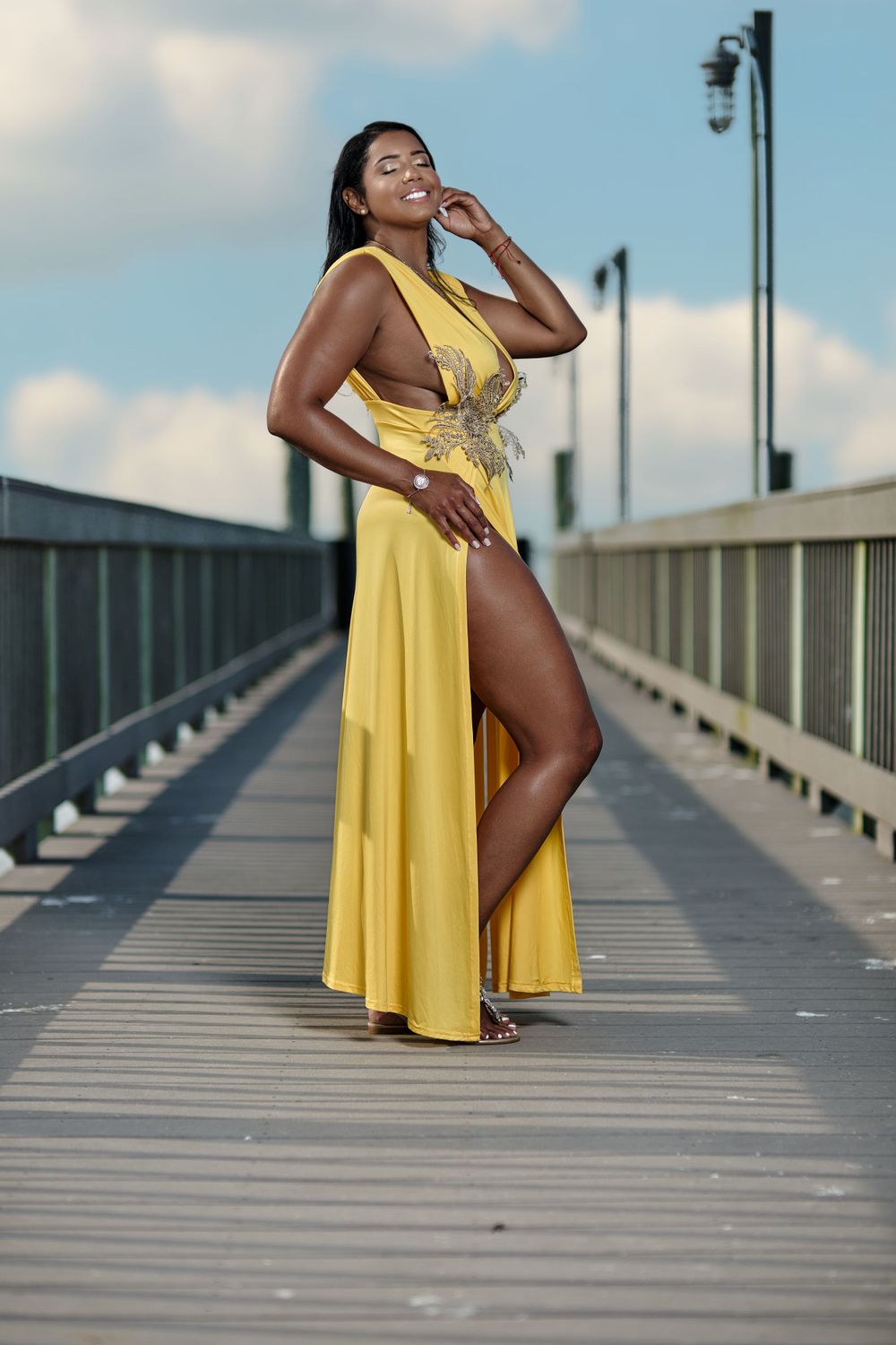 Striking pose in yellow flowing dress on wooden pier during bright summer day.